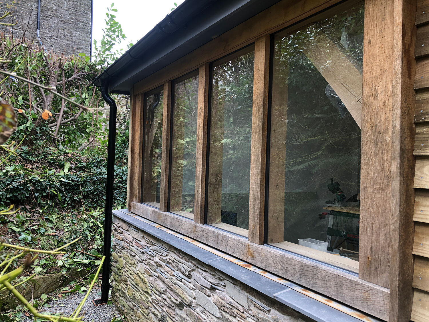 Green oak framed windows with stone wall and drainpipe