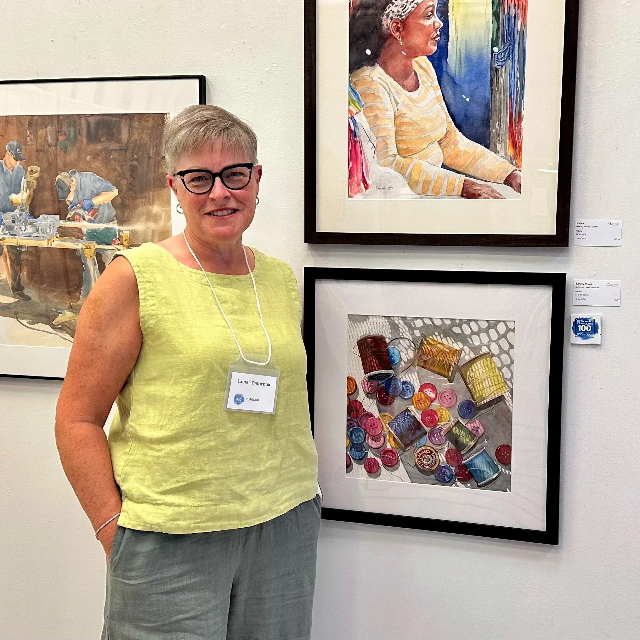 Laurel Onfrichuk standing next to her painting of colourful buttons and spools of thread.