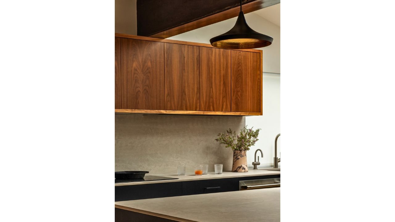 A detailed view of the Mallard Cove kitchen highlights richly grained wood cabinetry, streamlined countertops, and a modern sink area. Integrated lighting and restrained finishes reinforce the remodel’s warm contemporary material palette.