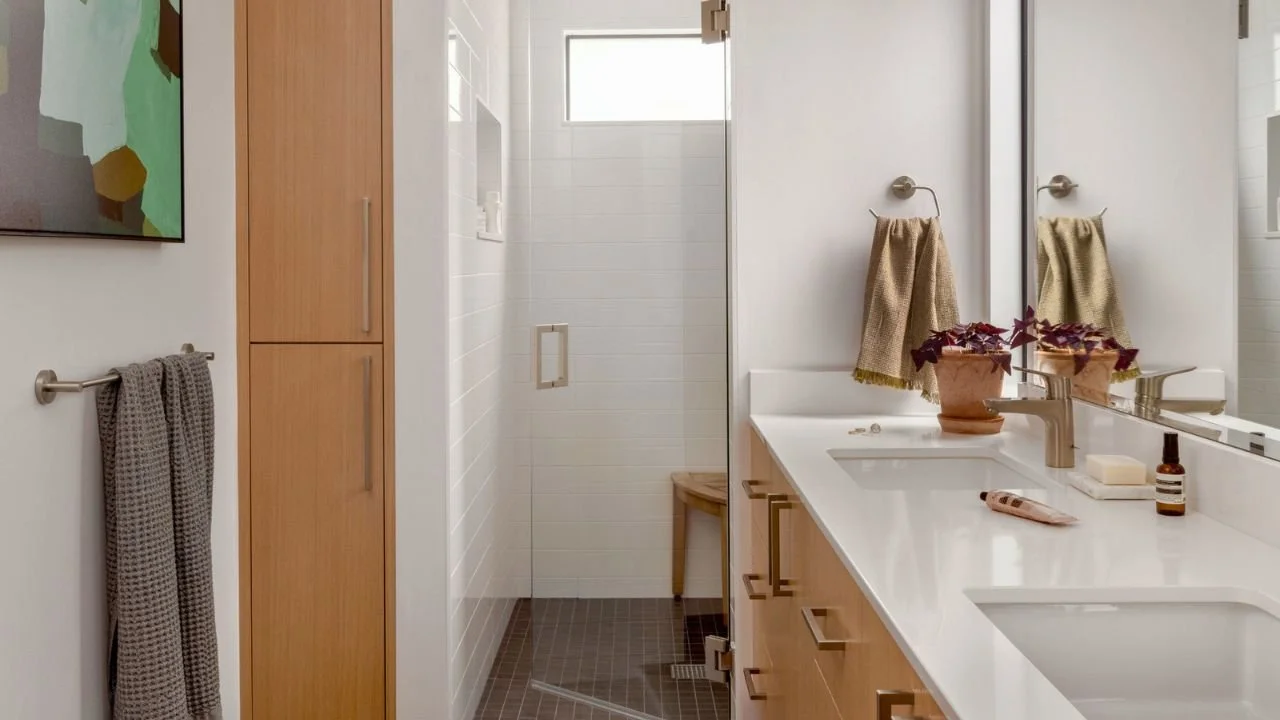 The Mallard Cove primary bathroom features a long double vanity, light wood cabinetry, a glass-enclosed walk-in shower, and bright natural light. Clean finishes and generous storage create a calm, functional retreat within the floating home.