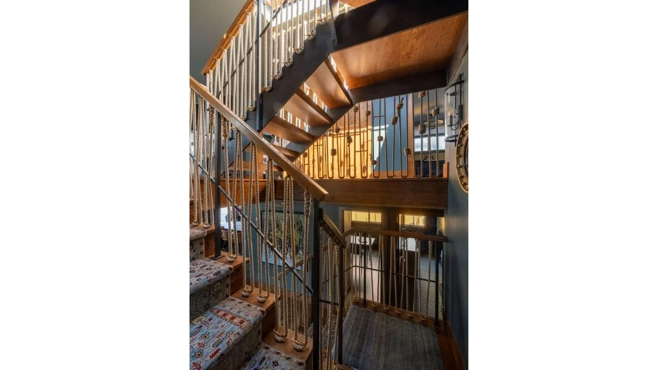 The Nesika Chuck Floating Home features a sculptural central staircase with open wood treads, slender railings, and warm integrated lighting. The stair connects multiple levels while serving as a defining architectural feature within the compact inte