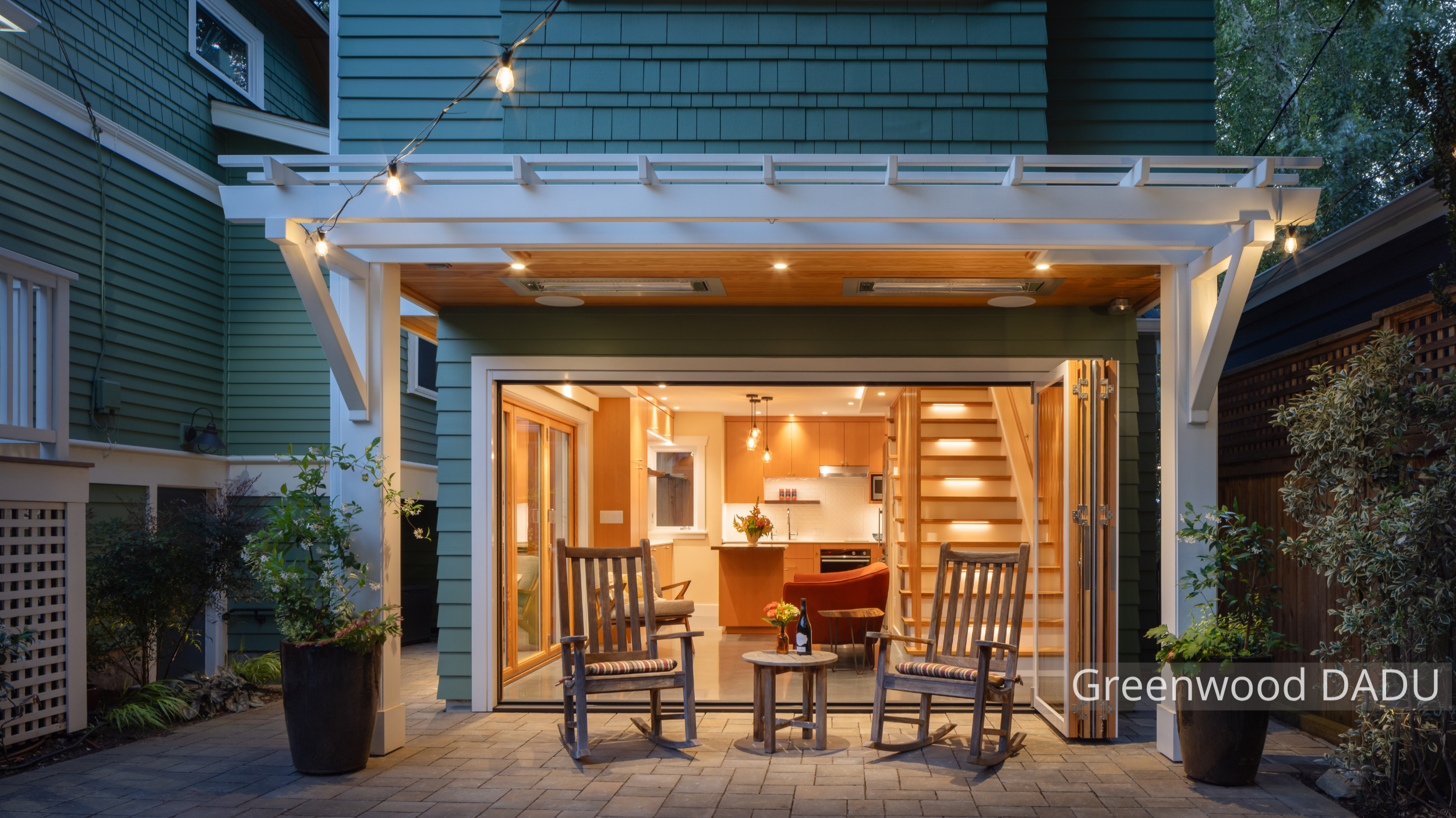 Exterior view of a modern detached accessory dwelling unit (DADU) in Seattle’s Greenwood neighborhood, featuring large folding glass doors that open the living room to a private backyard patio. The compact 660 sq ft structure replaces a former garage