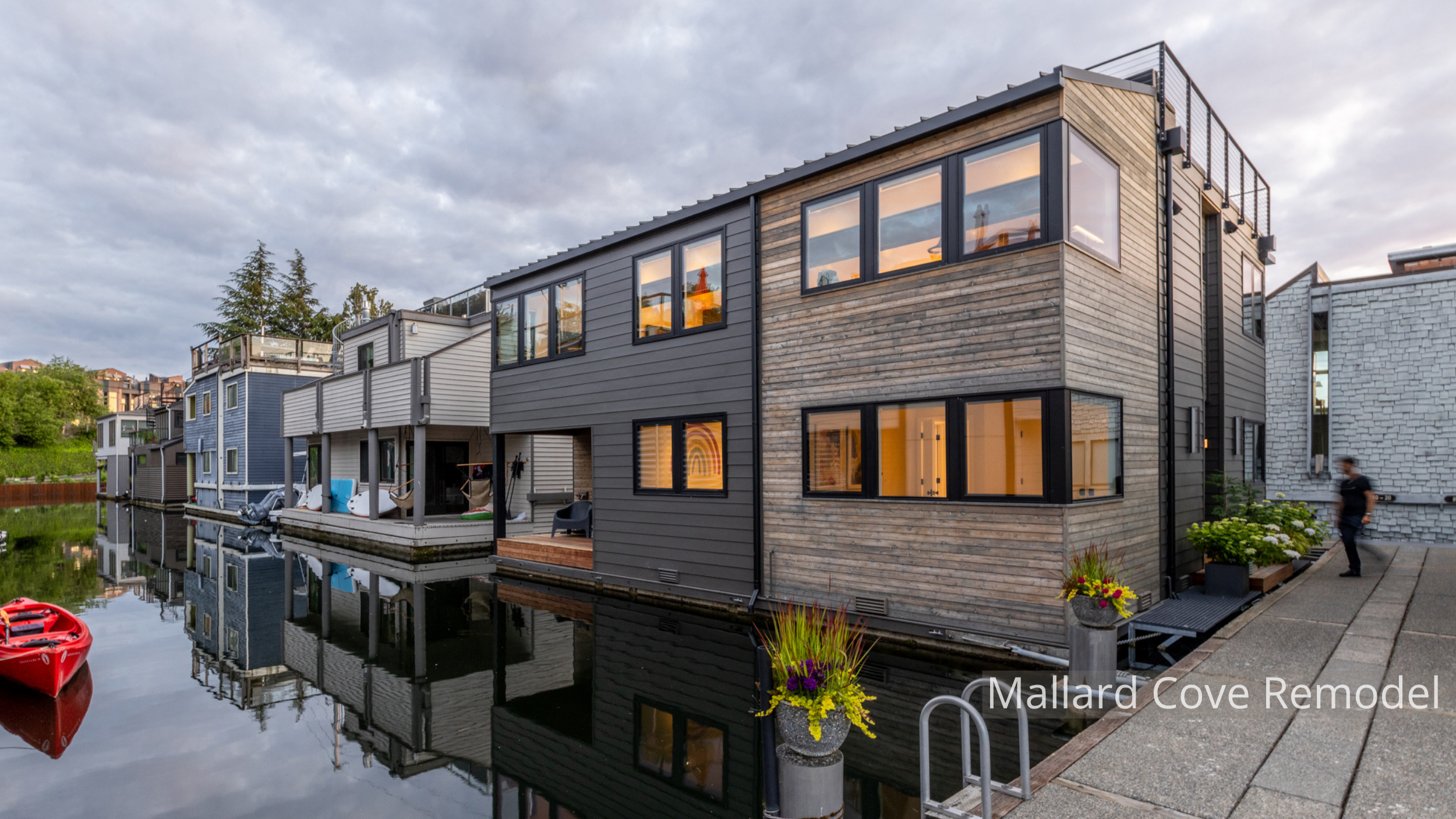 Mallard Cove floating home remodel featuring a refreshed contemporary exterior with natural wood siding, dark horizontal cladding, expansive windows, and a rooftop deck. The updated design brings warmth and modern character to the waterfront residenc