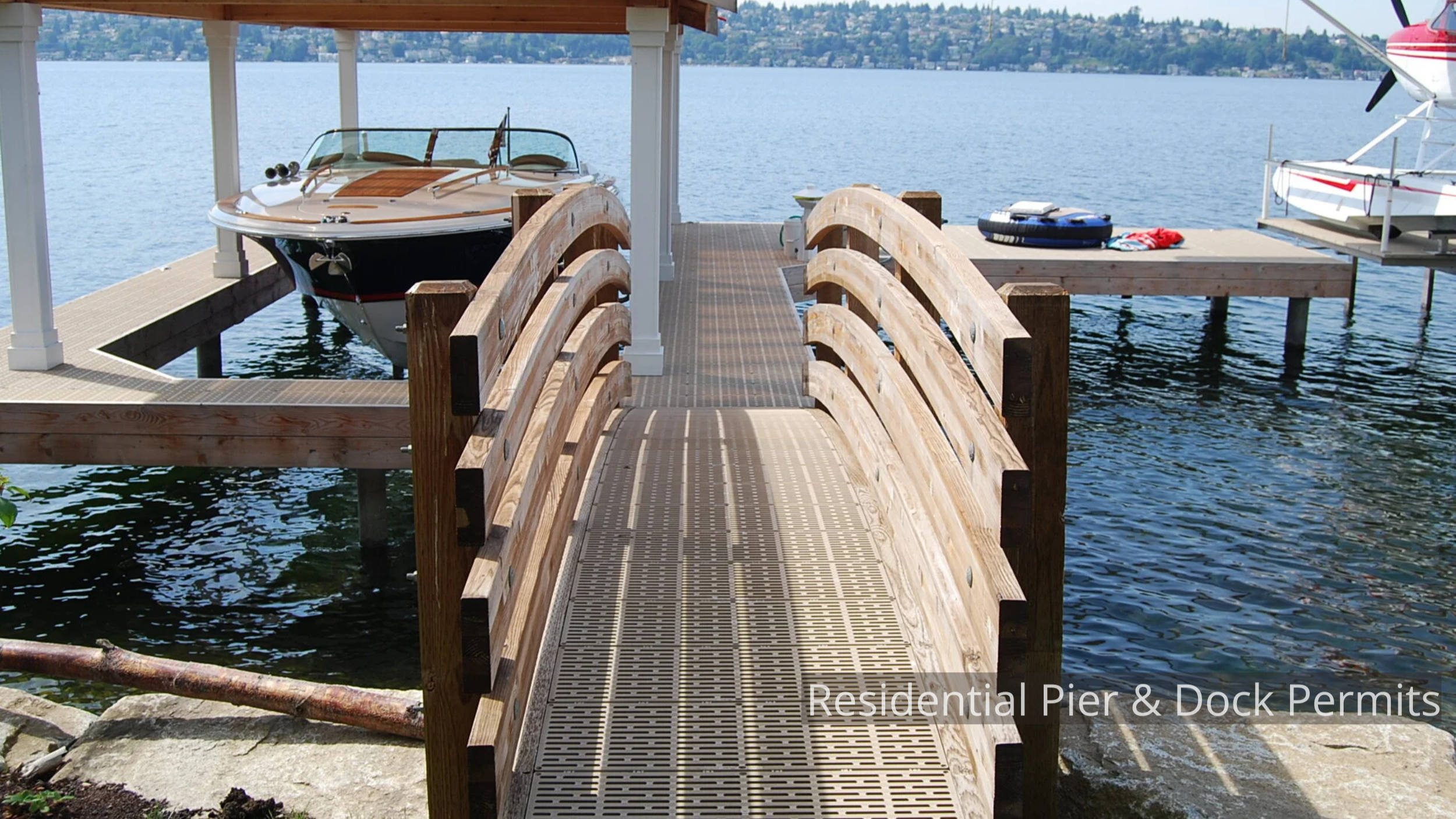 Wooden dock with a ramp leading to a covered boathouse on a lake, with boats and watercraft nearby.