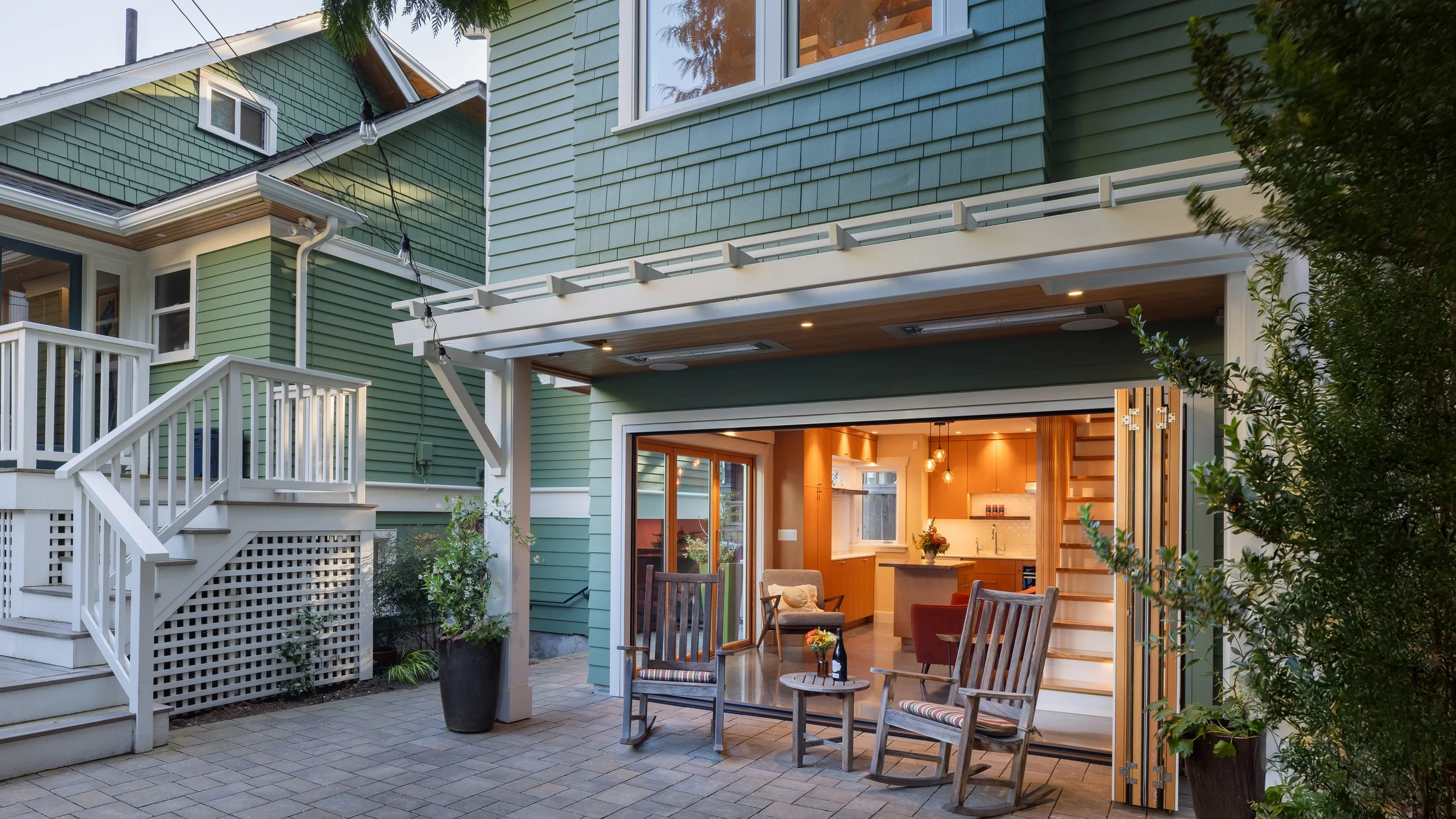 Exterior view of a backyard Seattle DADU designed to complement the main residence, featuring folding glass doors that open the living space to a private patio. The detached accessory dwelling unit replaces a former garage and integrates seamlessly w