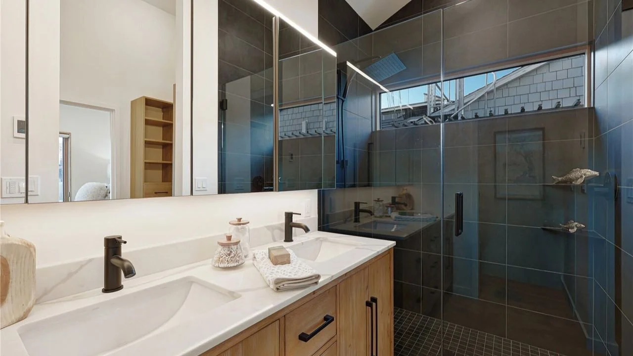 Primary bathroom in the Furhman Floating Home with a double vanity, light wood cabinetry, matte black fixtures, and a glass-enclosed shower. The clean, modern design creates a bright and calming ensuite retreat.