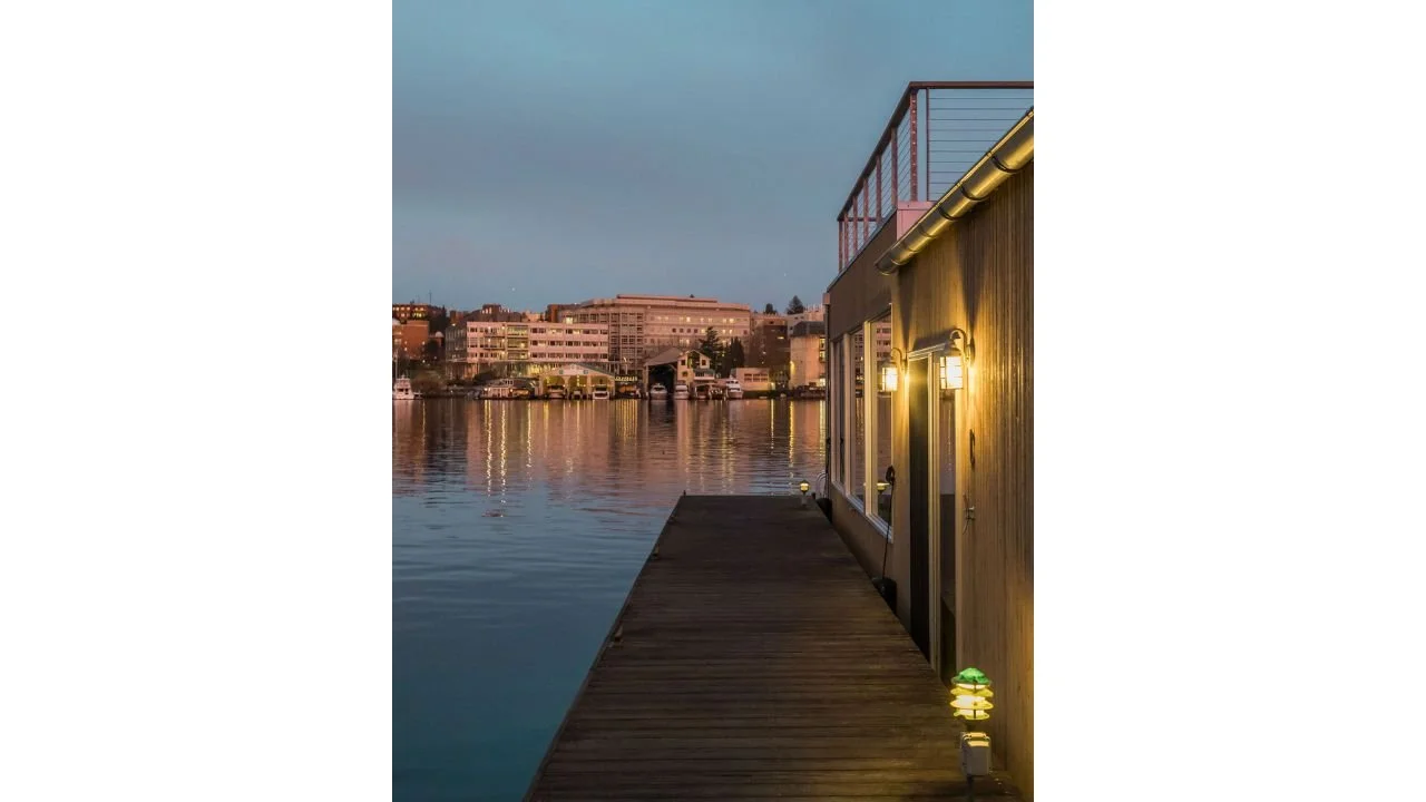 Side dock view of the Furhman Floating Home captured at dusk, highlighting the dock edge, exterior lighting, and quiet waterfront atmosphere. The composition reflects the calm, immersive experience of floating home living.