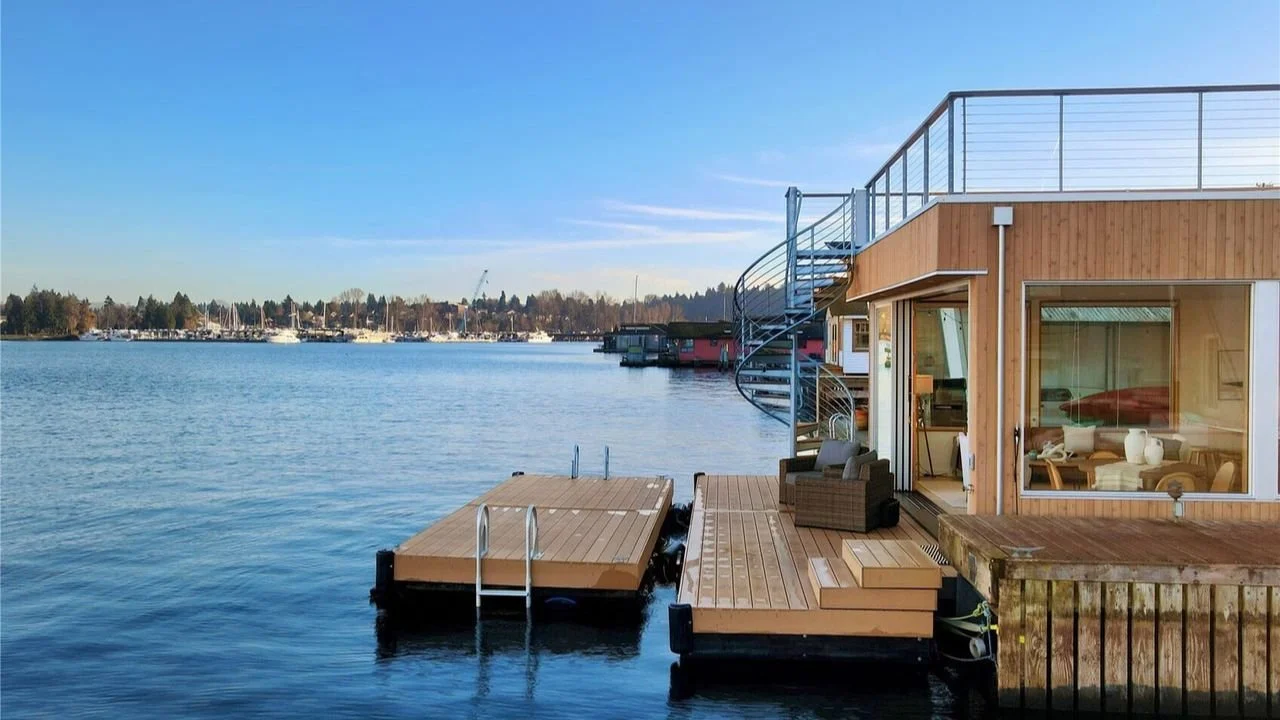 Daytime exterior of the Furhman Floating Home showing the dock, rooftop deck, and expansive waterfront glazing. The composition highlights the home’s layered outdoor spaces and modern floating architecture.