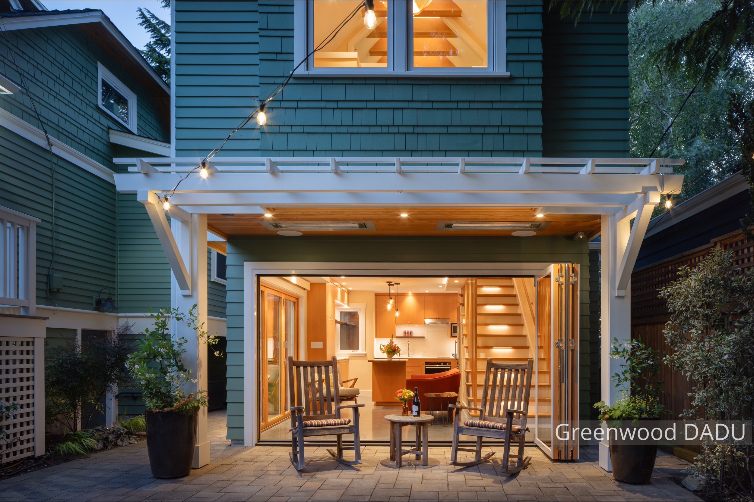 Exterior view of a modern detached accessory dwelling unit (DADU) in Seattle’s Greenwood neighborhood, featuring large folding glass doors that open the living room to a private backyard patio. The compact 660 sq ft structure replaces a former garage