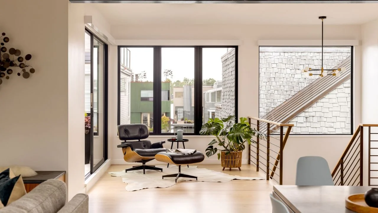 A bright upper-level lounge in the Mallard Cove Remodel is framed by large windows and an open staircase with contemporary cable railings. Light wood flooring and carefully placed furnishings create an airy transition between the home’s living spaces