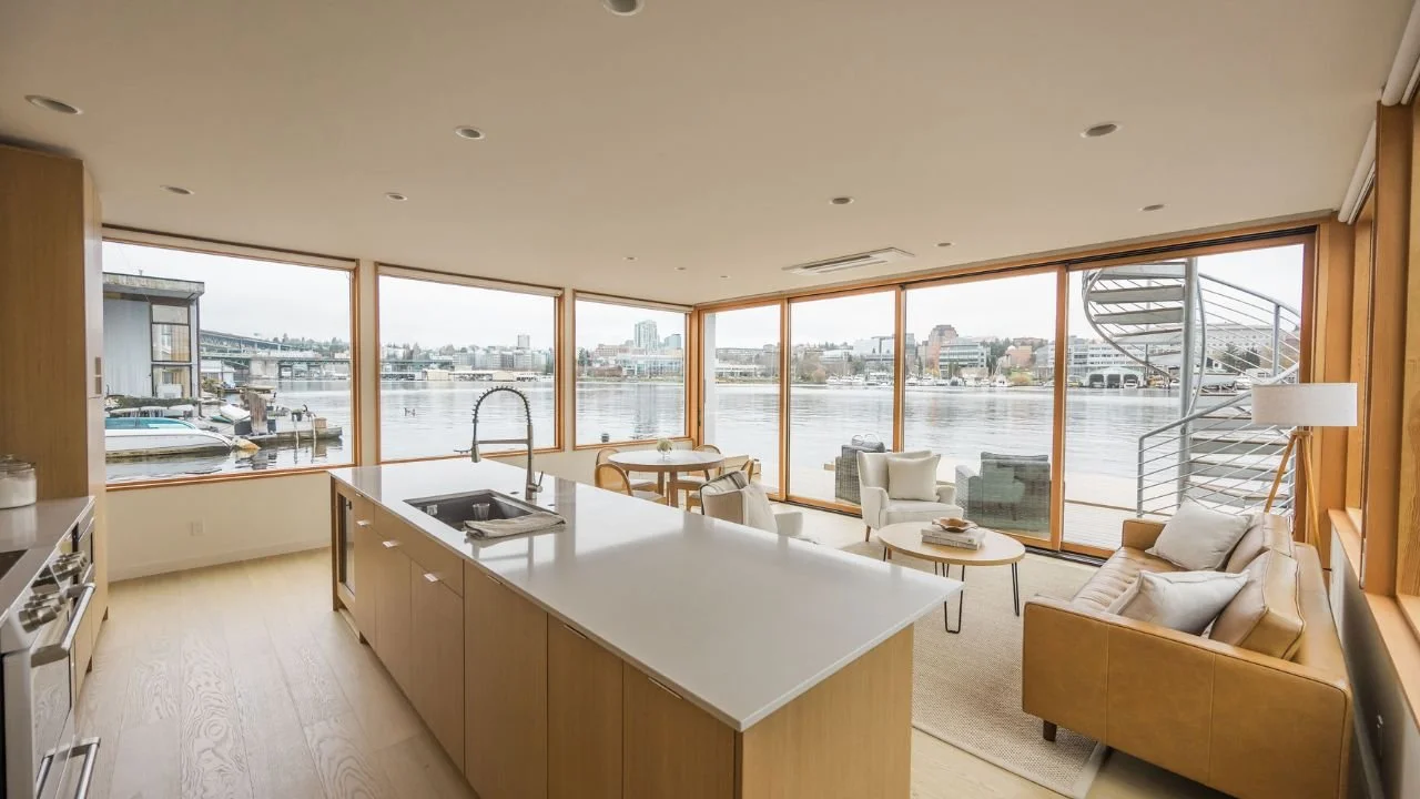 Bright kitchen in the Furhman Floating Home with a streamlined island, corner windows, and a cozy sitting area oriented to Portage Bay. The design combines functionality with uninterrupted waterfront views.