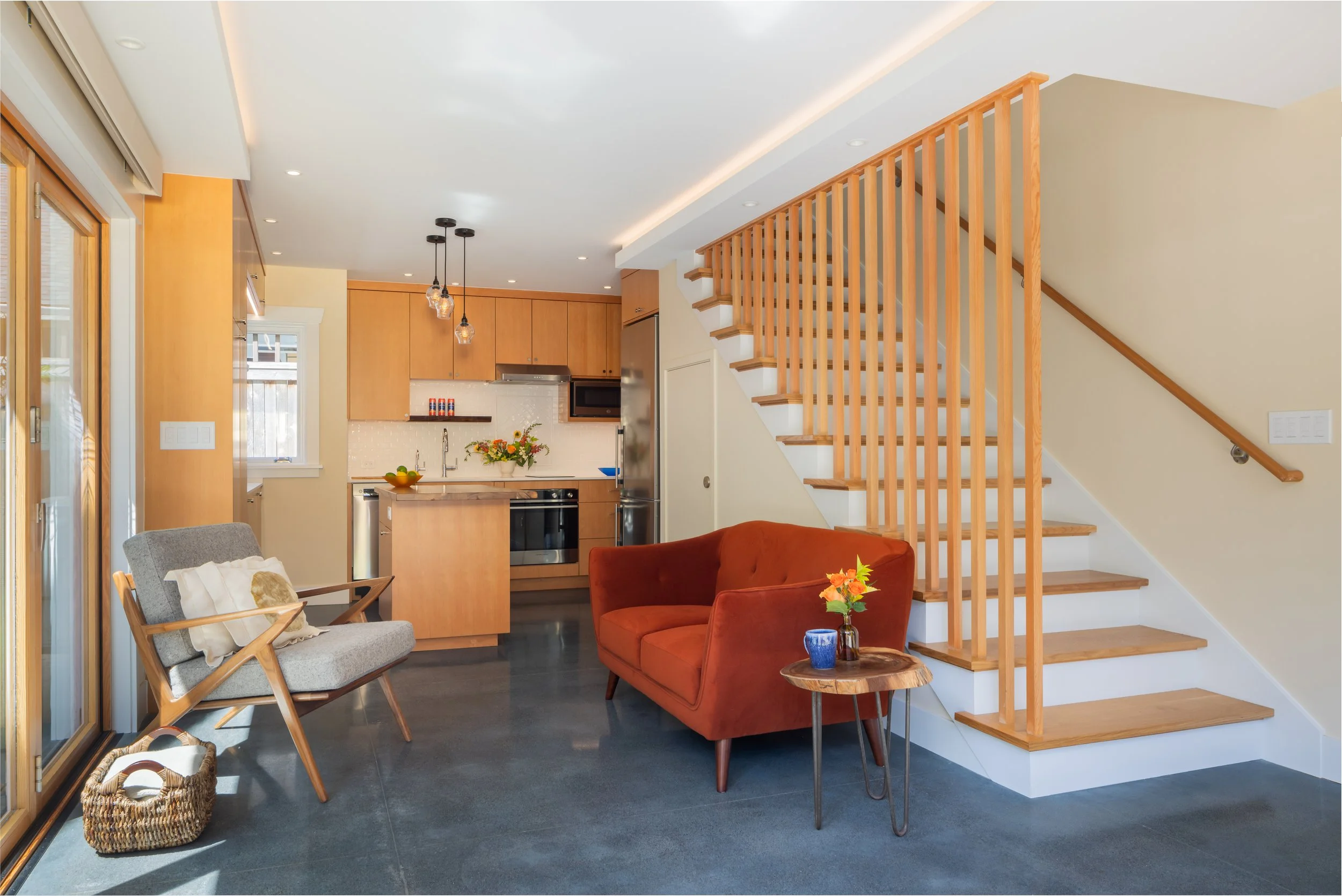 Interior view of a modern Seattle DADU showcasing an open-concept living area with compact kitchen, custom wood staircase, and efficient small-space layout. The design emphasizes natural light, clean lines, and functional flow, with direct access to 