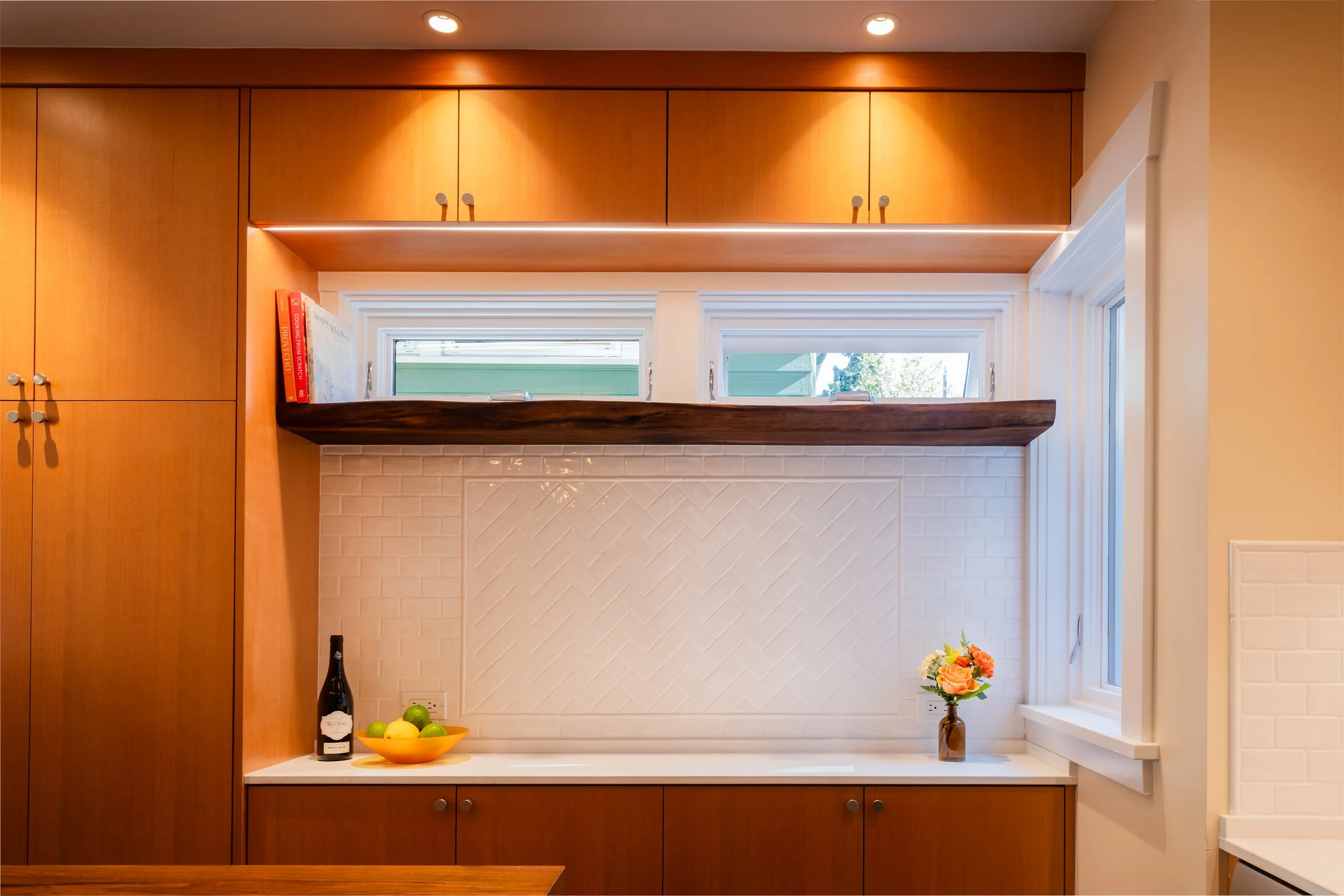Custom kitchen cabinetry detail in a Seattle DADU featuring warm wood cabinets, integrated storage, and a minimalist backsplash with open wood shelving. A horizontal window brings in natural light while maintaining privacy, enhancing the clean and ef