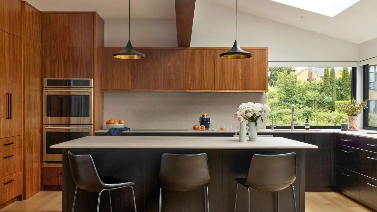 The remodeled kitchen features extensive wood cabinetry, a large contrasting island, integrated appliances, and broad windows overlooking greenery. Generous seating and workspace make the kitchen a functional center for cooking, gathering, and entert
