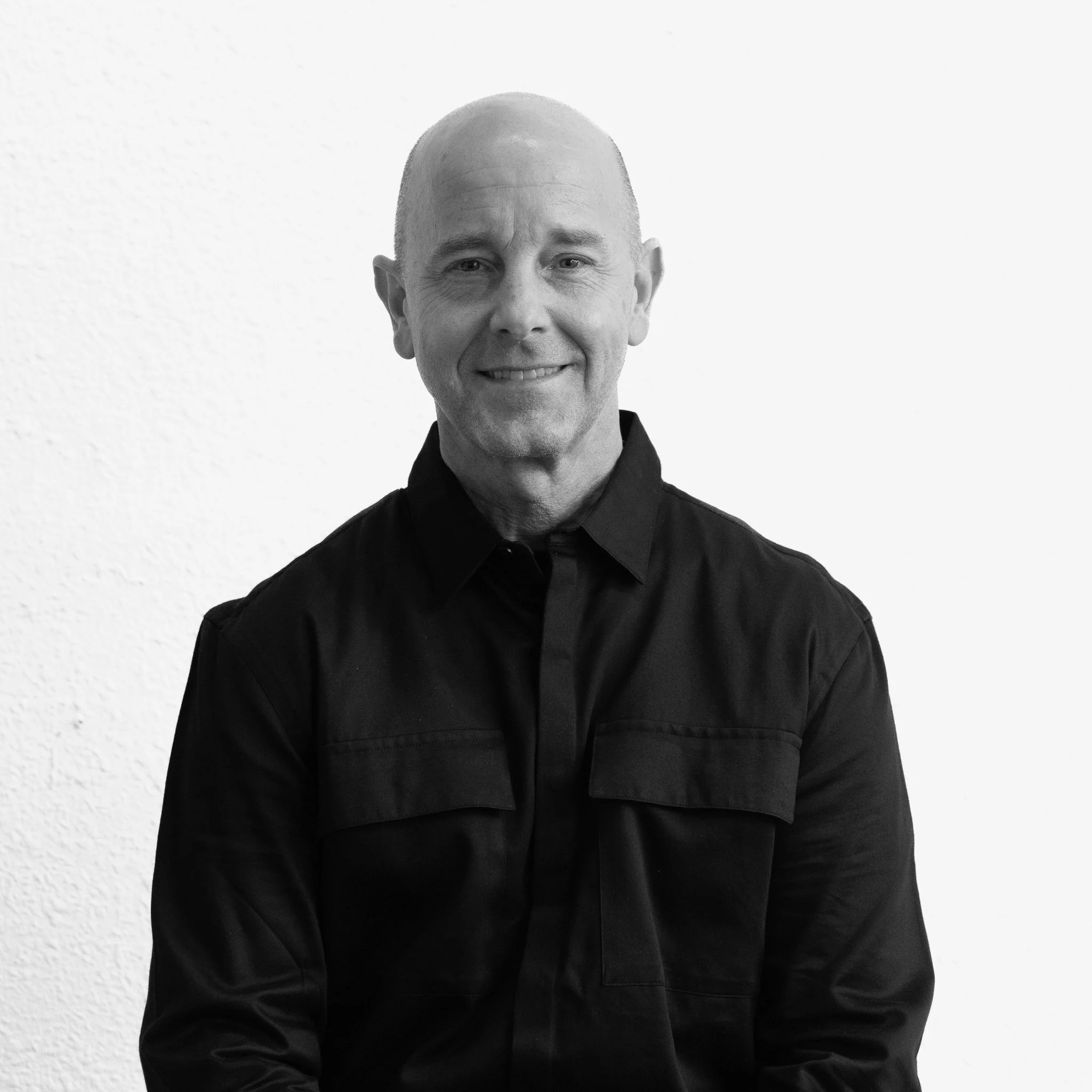 Black and white portrait of Troy Hussing smiling at the camera against a plain wall background.