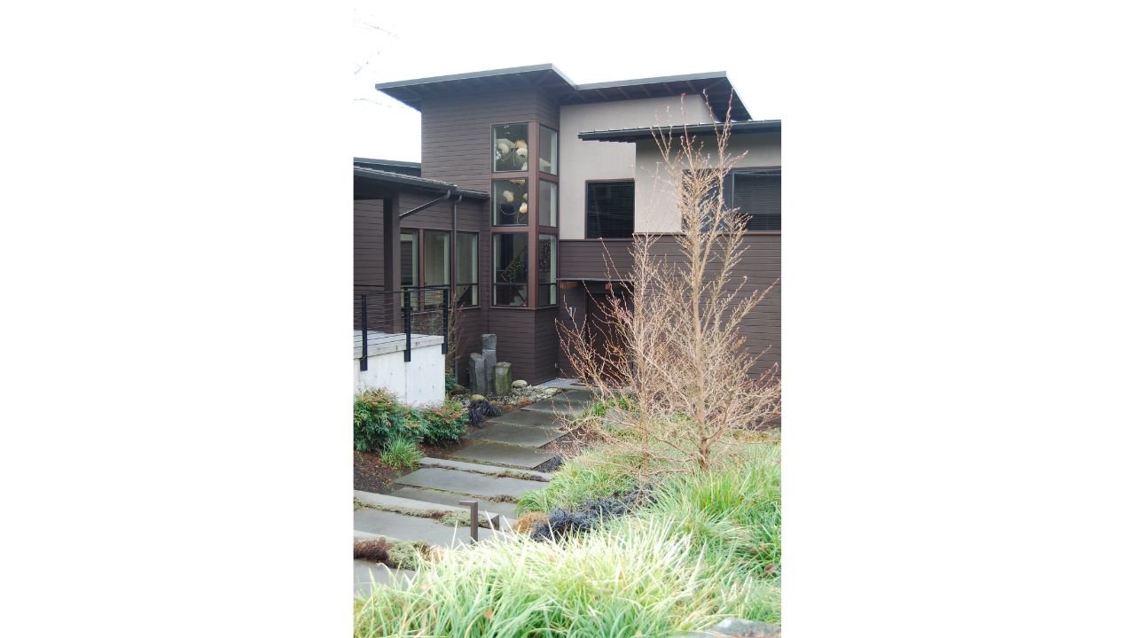 A garden-facing portion of the Lake Washington New Home combines broad rooflines, warm wood siding, and windows positioned toward the landscaped grounds. Layered planting beds soften the architecture and strengthen the connection between the interior