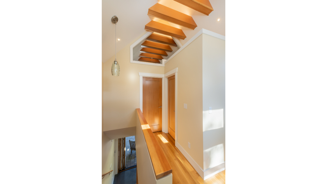 Upper-level hallway in a Seattle DADU featuring a vaulted ceiling with exposed wood beams, natural light, and warm wood flooring. The design emphasizes vertical volume and architectural detail while connecting private spaces within the compact layout