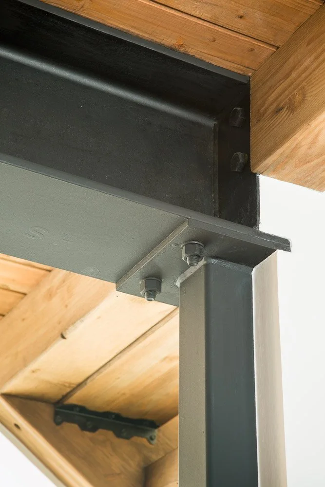 Close-up of metal and wooden structural framing showing bolts and attachment points in a building interior.