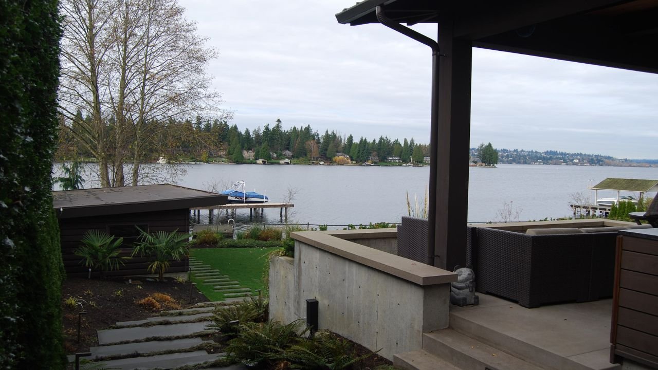 A covered outdoor terrace frames an expansive view across Lake Washington. Deep roof overhangs, built-in seating, and direct access to the garden create a comfortable outdoor room for relaxing and gathering beside the water.