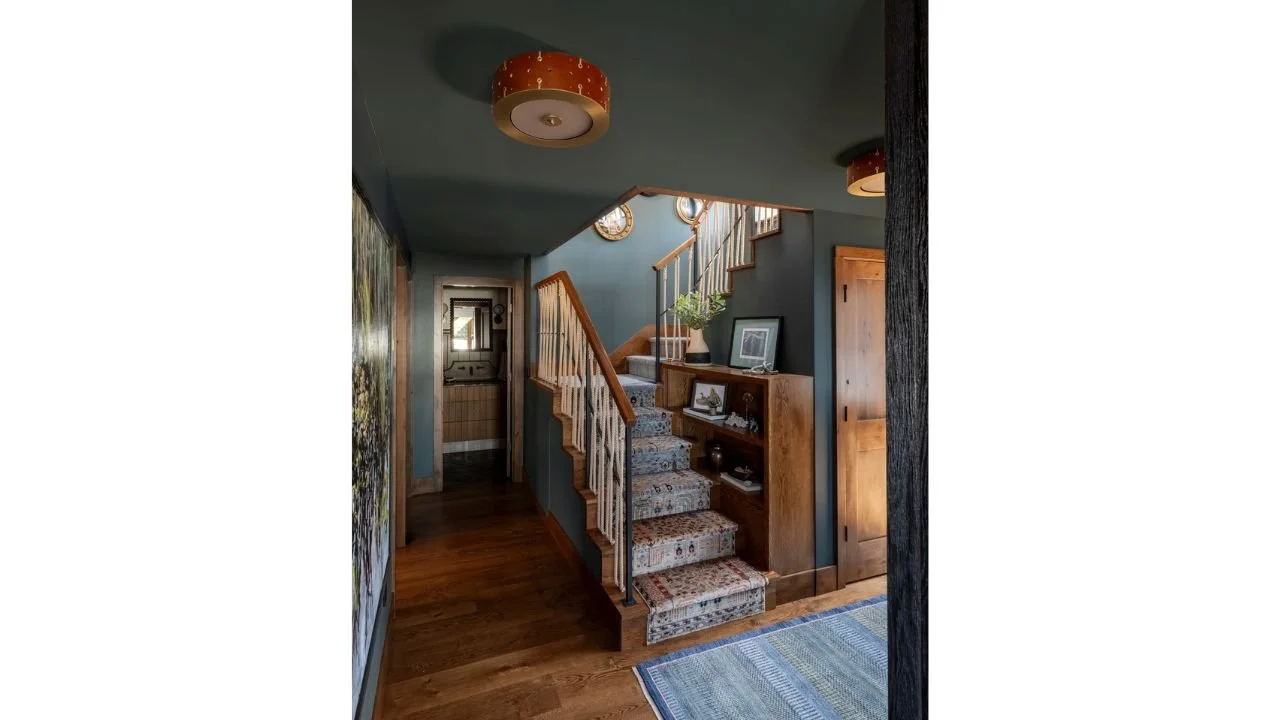 The entry hall of the Nesika Chuck Floating Home features deep blue walls, warm wood flooring, patterned stair treads, and integrated shelving. The compact circulation space introduces the home’s rich color palette and guides movement toward the uppe