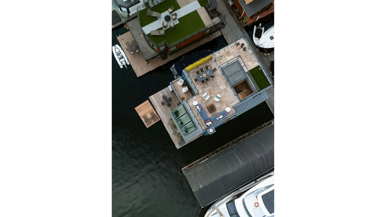 An aerial view of the Nesika Chuck Floating Home highlights its spacious rooftop terrace, outdoor seating, planted roof areas, and position within the waterfront community. The roof design expands usable living space while maximizing sunlight and pan