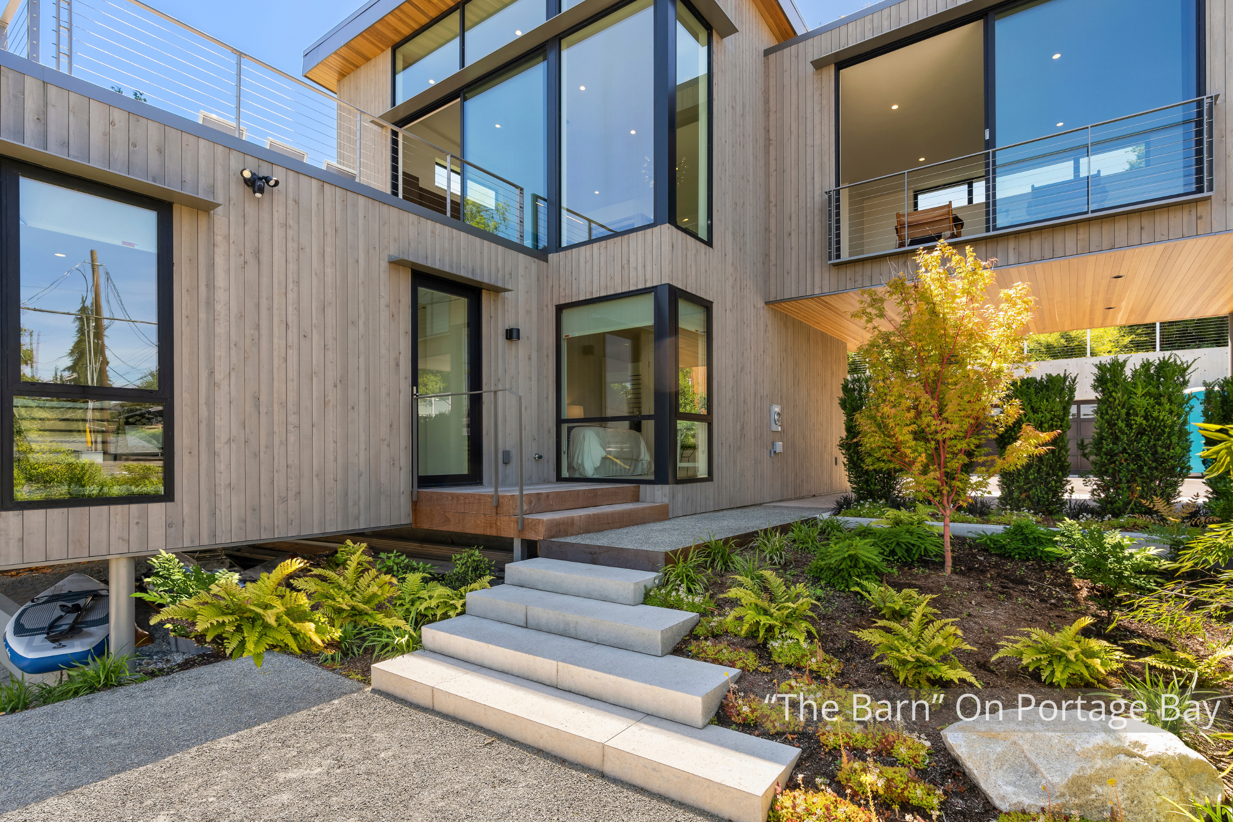The "Barn" on Portage Bay is a contemporary waterfront residence defined by its dramatic gabled form, expansive floor-to-ceiling glass, and warm natural wood detailing. Large windows fill the home with natural light while connecting the interior to t