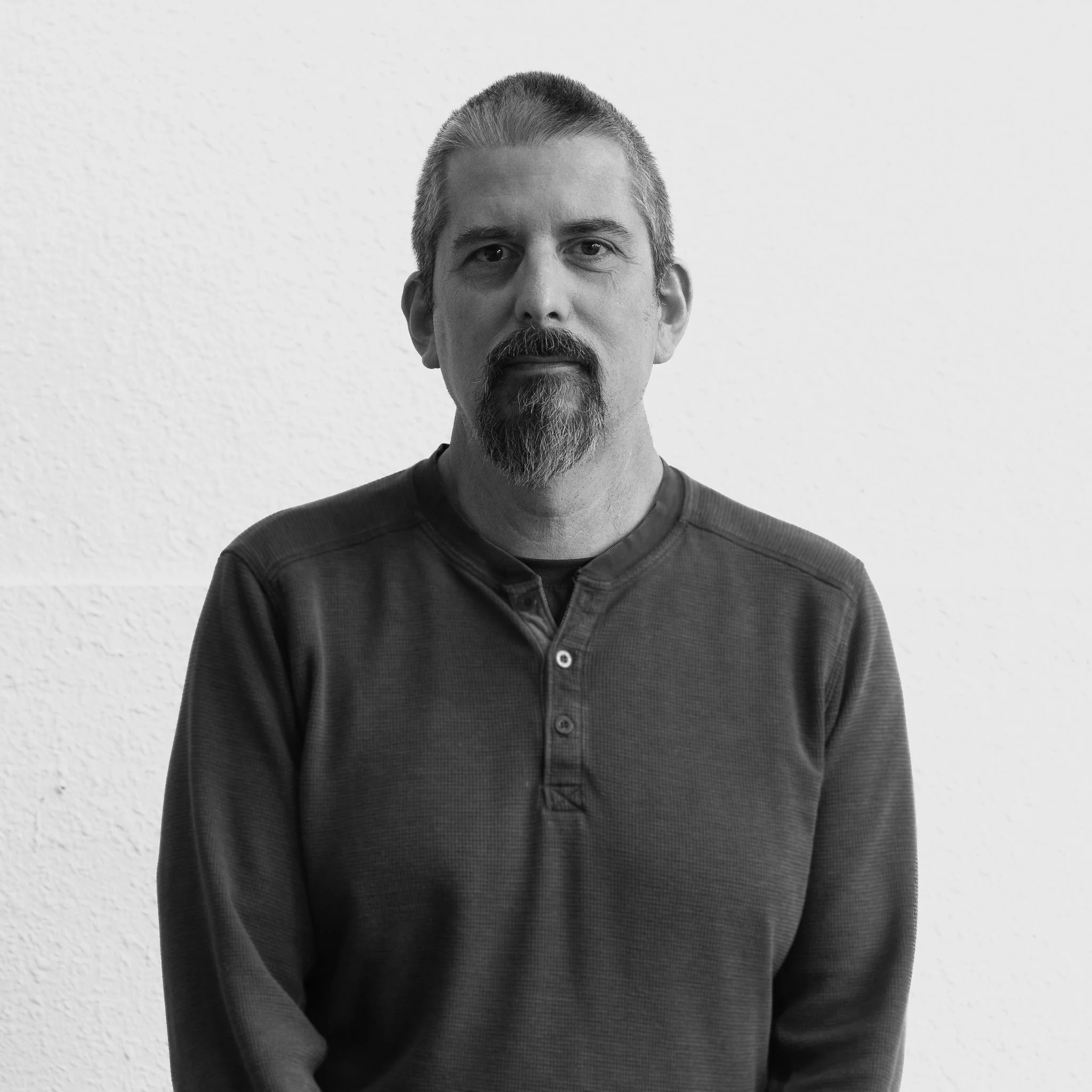 Black and white portrait of John Pasco standing against a plain wall.