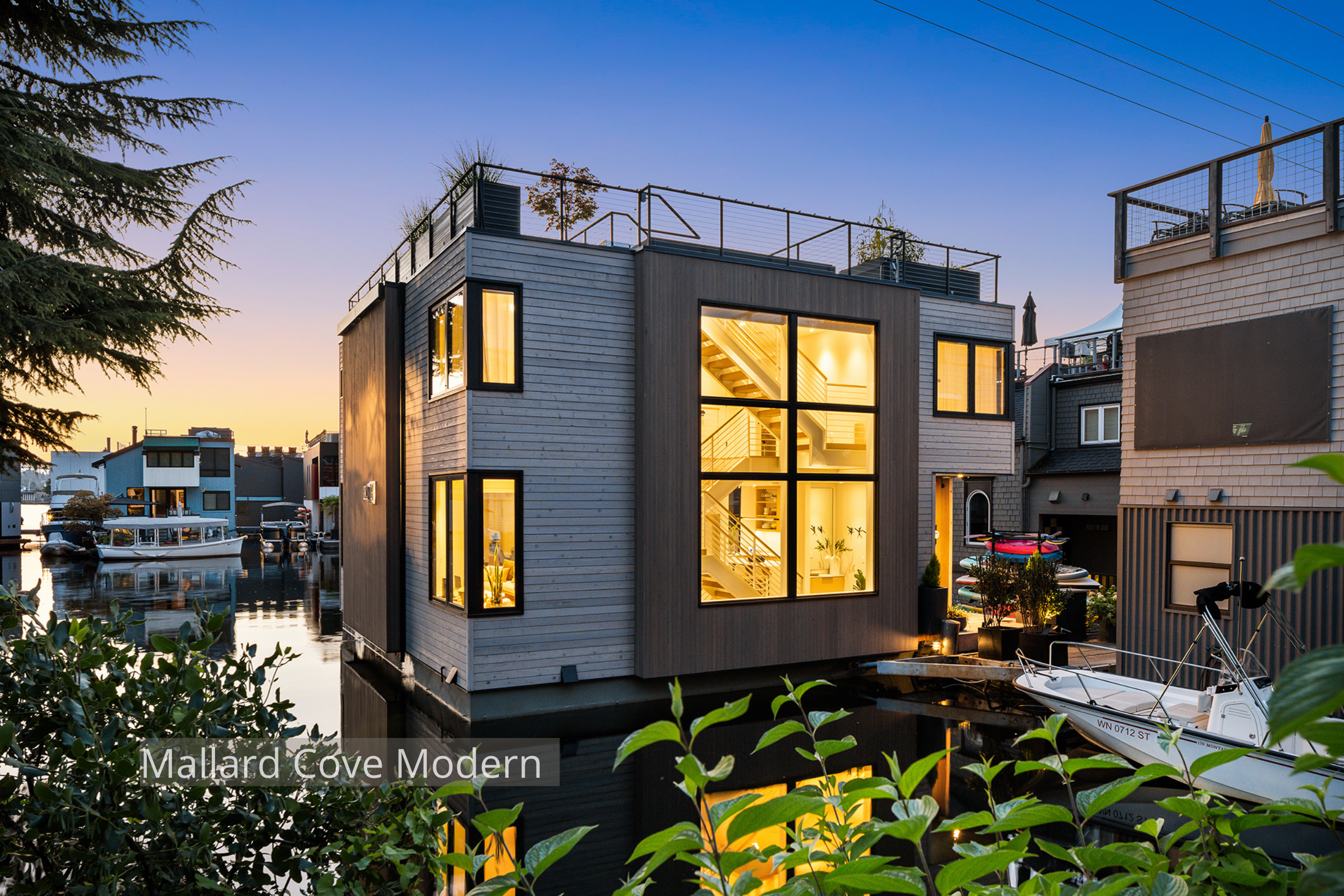 Lake Union modern floating home designed by ECCO Architecture in Seattle, featuring expansive floor-to-ceiling windows, sliding glass doors, and multiple outdoor living areas including a main-level deck, accessory float, and rooftop deck. This contem