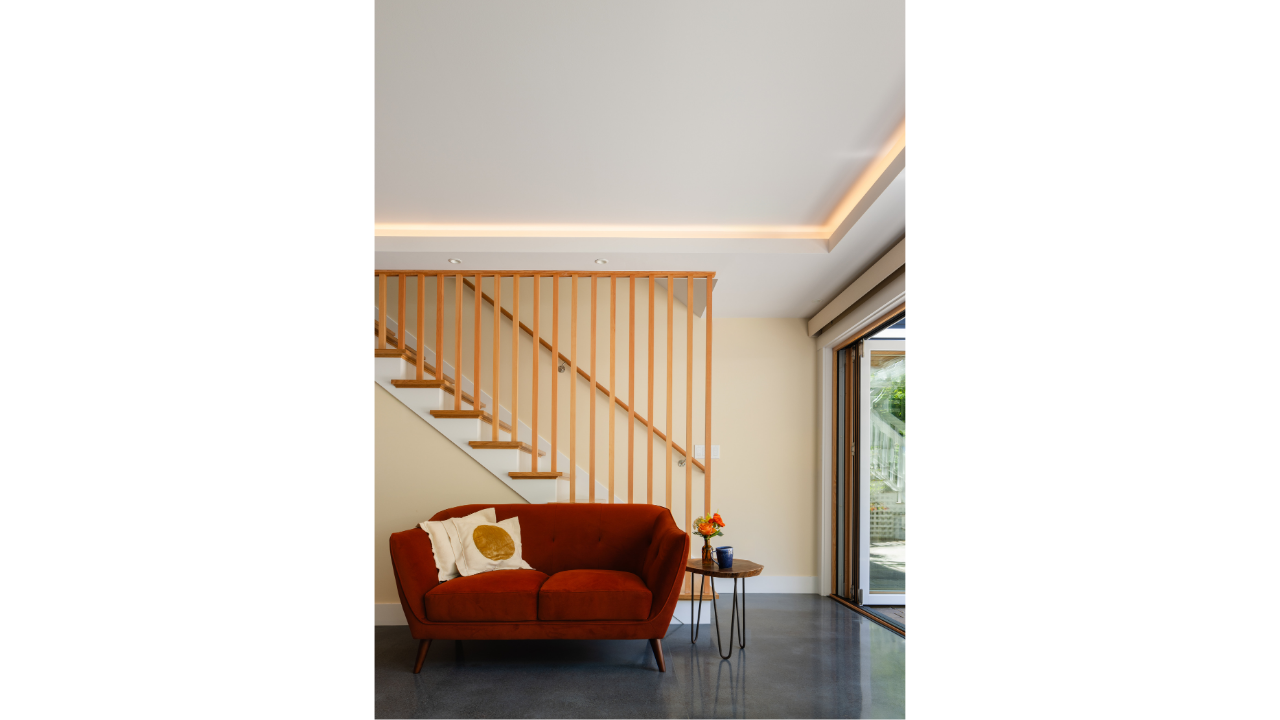 Interior detail of a modern Seattle DADU featuring a custom wood staircase with vertical slat railing, integrated lighting, and a compact living area. The design emphasizes clean lines, warm materials, and efficient use of space, with natural light e