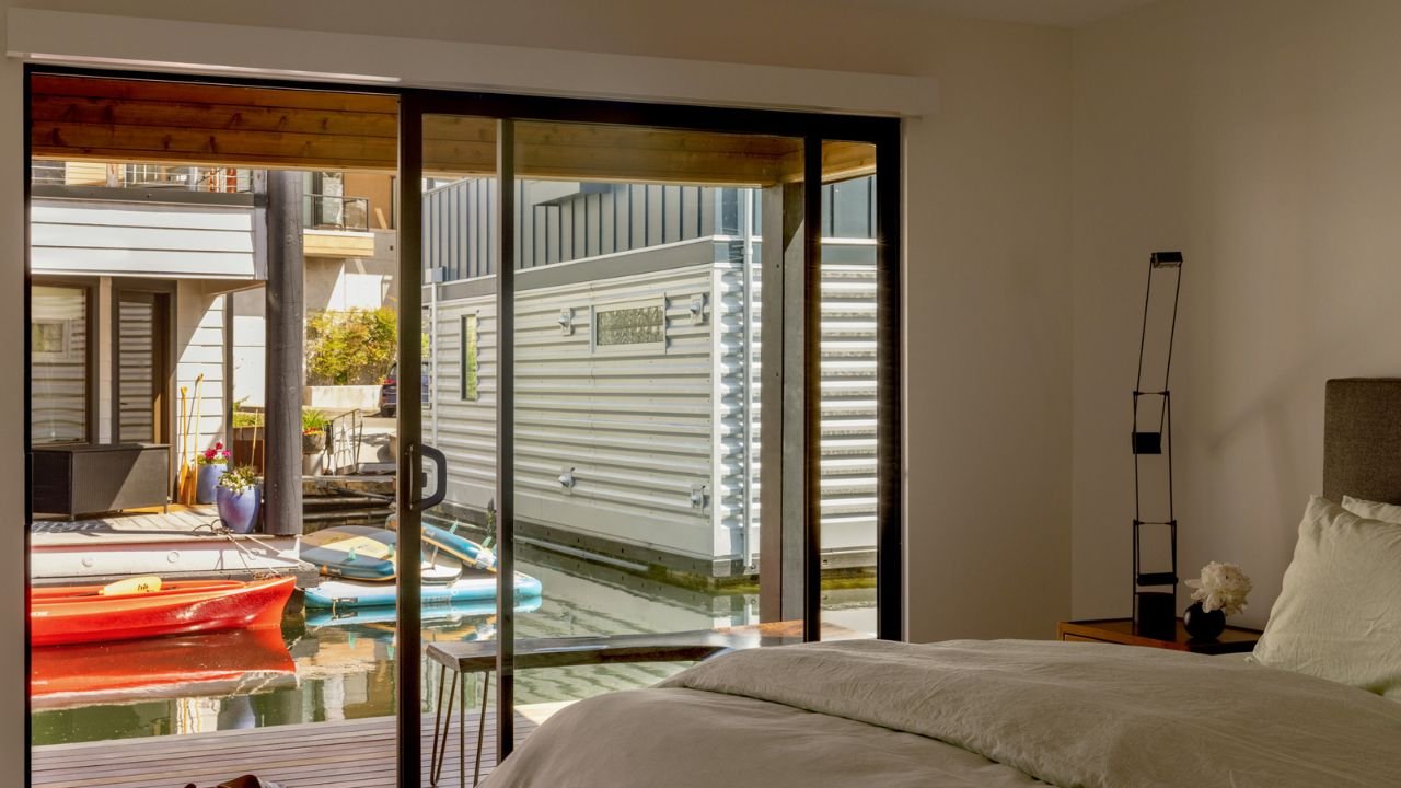 A bedroom in the Mallard Cove Remodel opens toward the dock through wide sliding glass doors. Natural light, water views, and direct visual connection to neighboring boats make the compact room feel open and closely connected to waterfront life.