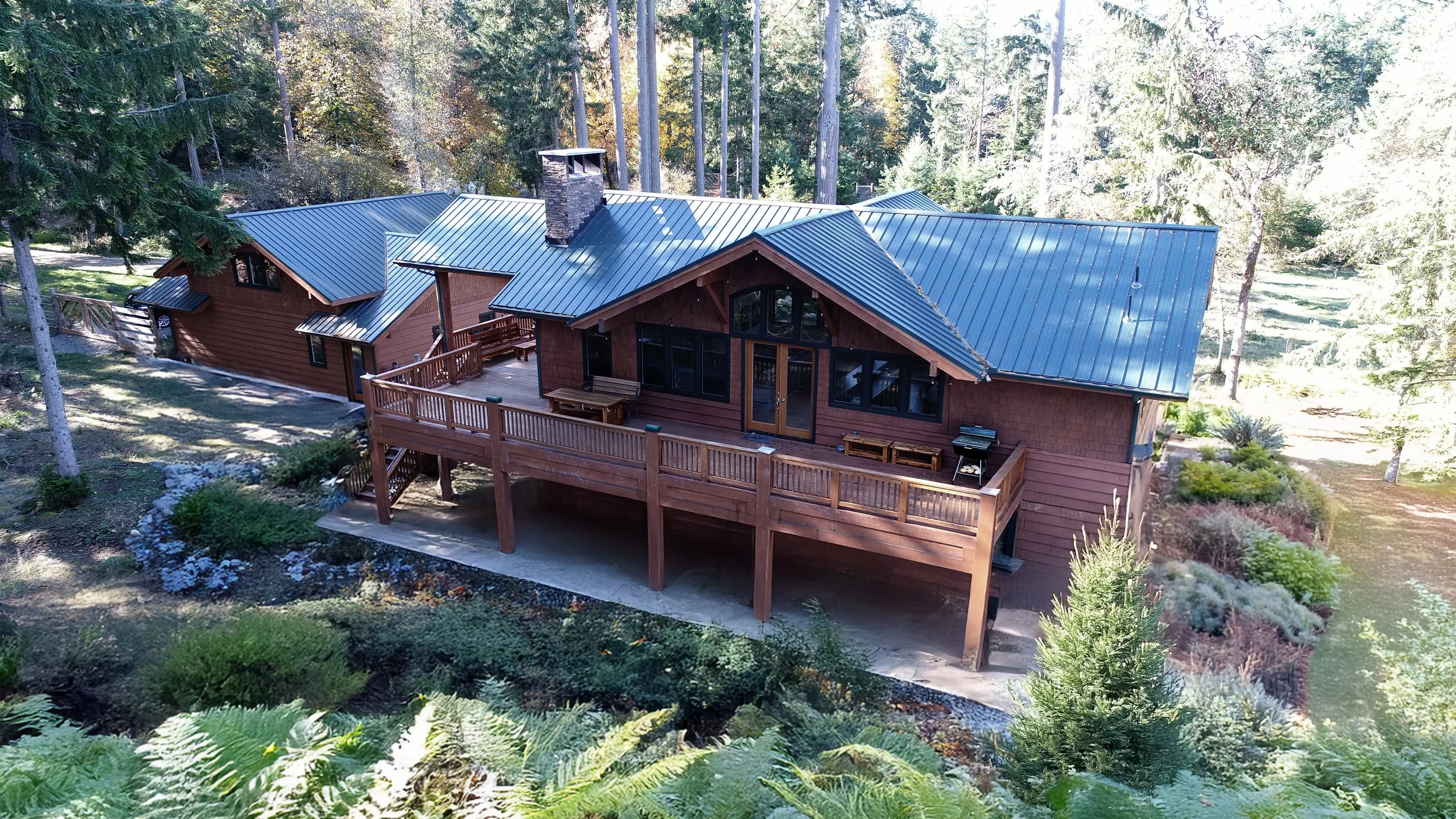 Contemporary craftsman-style home with cedar siding, metal roof, and raised deck integrated into a forested Pacific Northwest site