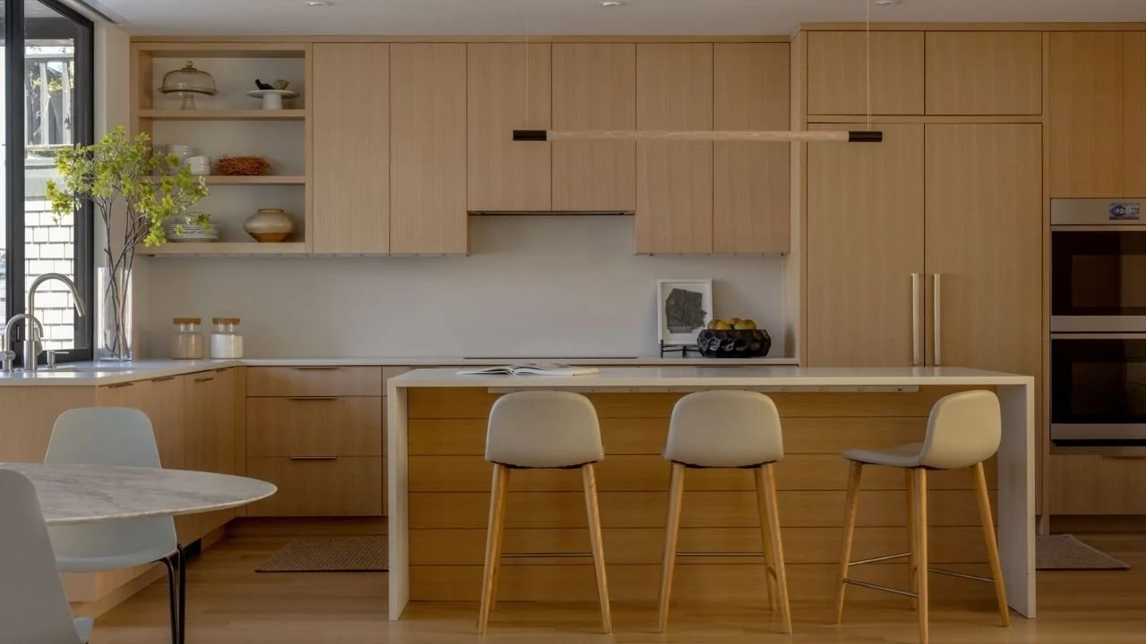The Mallard Cove Modern kitchen features full-height light wood cabinetry, integrated appliances, and a generous island with counter seating. Clean lines and efficient storage create a calm, functional workspace suited to the compact floating-home fl