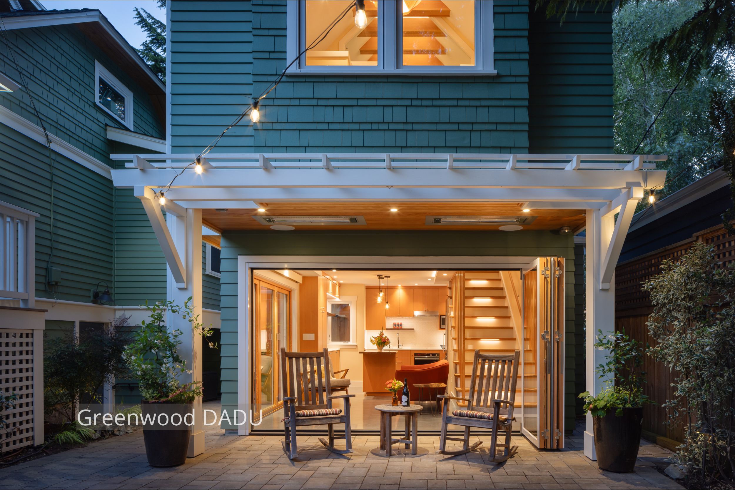 Exterior view of a modern detached accessory dwelling unit (DADU) in Seattle’s Greenwood neighborhood, featuring large folding glass doors that open the living room to a private backyard patio. The compact 660 sq ft structure replaces a former garage