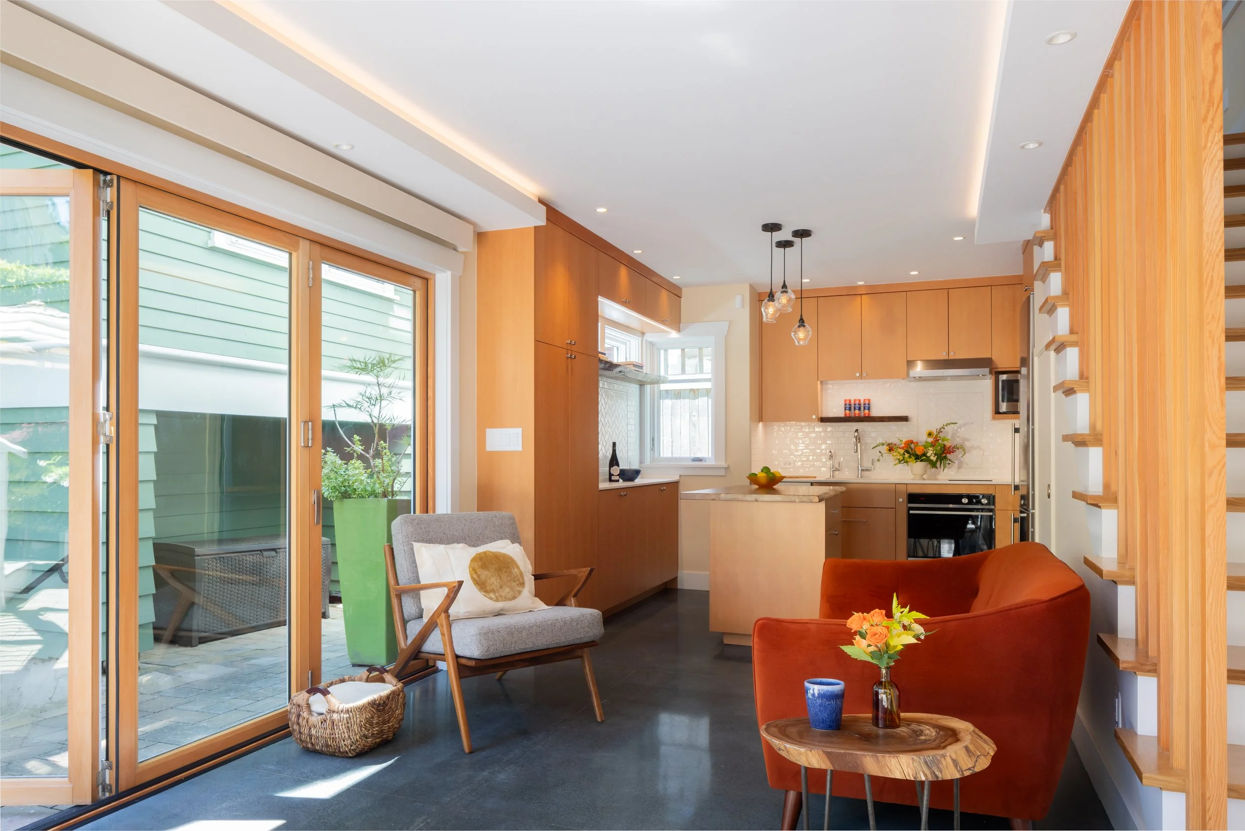 Interior view of a compact Seattle DADU highlighting a modern kitchen with warm wood cabinetry, open shelving, and efficient layout integrated into a small-space living area. Natural light enters through large sliding glass doors, strengthening the c