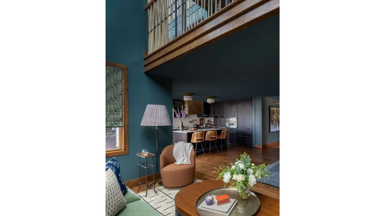 An open living area connects directly to the kitchen beneath the upper-level loft of the Nesika Chuck Floating Home. Rich color, warm wood flooring, and carefully arranged furnishings create a welcoming interior while making efficient use of the comp