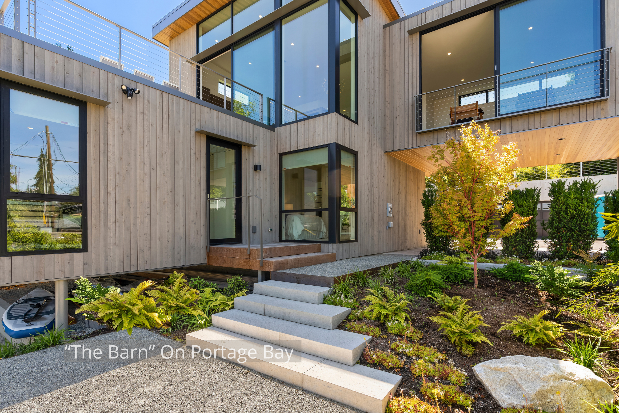 The "Barn" on Portage Bay is a contemporary waterfront residence defined by its dramatic gabled form, expansive floor-to-ceiling glass, and warm natural wood detailing. Large windows fill the home with natural light while connecting the interior to t
