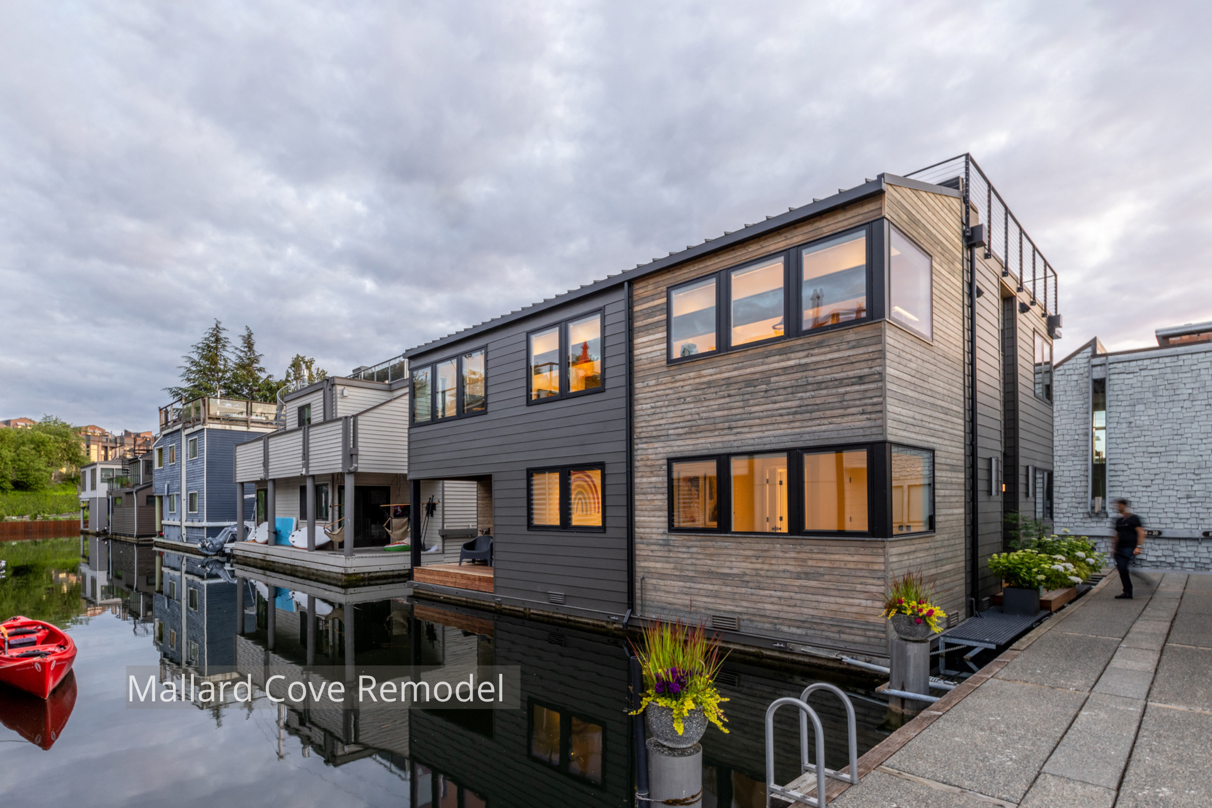 Mallard Cove floating home remodel featuring a refreshed contemporary exterior with natural wood siding, dark horizontal cladding, expansive windows, and a rooftop deck. The updated design brings warmth and modern character to the waterfront residenc