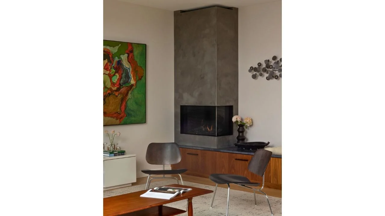 An intimate living area in the Mallard Cove Remodel is organized around a sculptural stone fireplace and warm wood cabinetry. Contemporary furnishings, artwork, and natural materials create a comfortable gathering space with a refined residential cha