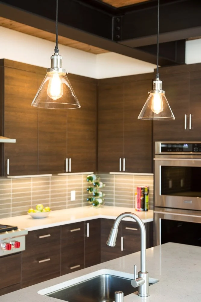 Modern kitchen with wooden cabinets, beige backsplash tiles, pendant lights, a sink with a gooseneck faucet, and stainless steel appliances.