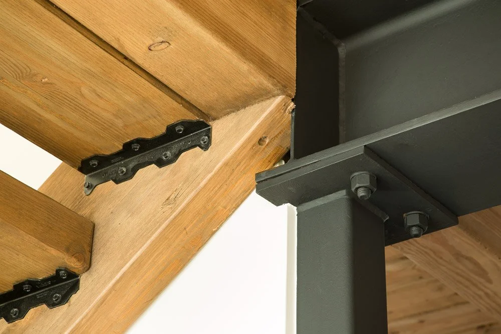 Close-up of a wooden staircase connected to a black metal support structure with bolts.