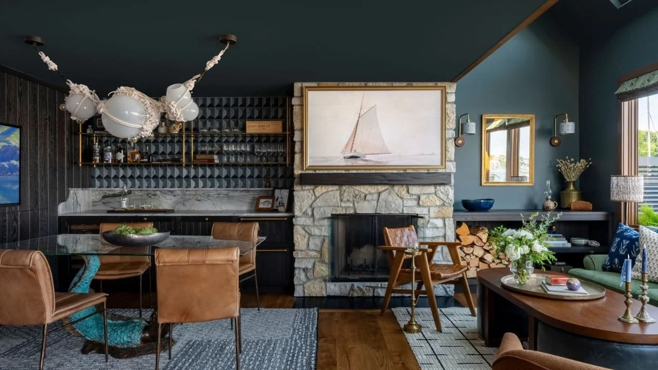 The Nesika Chuck great room brings together a stone fireplace, built-in bar, dining space, and comfortable lounge seating beneath deep teal walls. Layered textures and custom details create a warm, expressive interior suited to both everyday living a