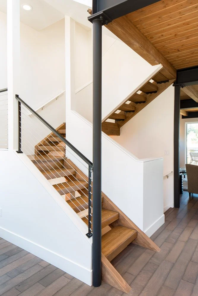 Interior view of a modern staircase with wooden steps, black metal railings, and white walls in a home.
