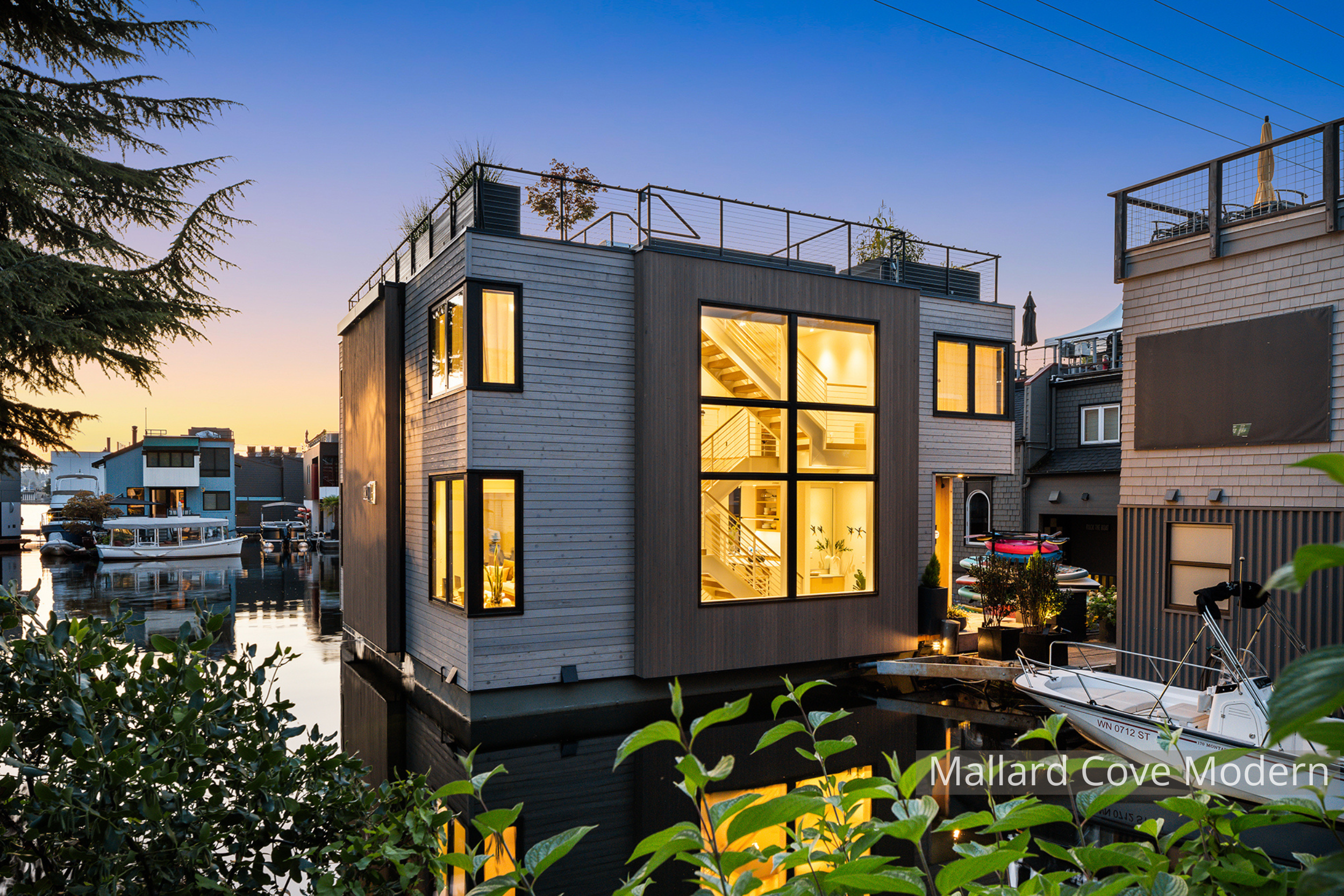Lake Union modern floating home designed by ECCO Architecture in Seattle, featuring expansive floor-to-ceiling windows, sliding glass doors, and multiple outdoor living areas including a main-level deck, accessory float, and rooftop deck. This contem