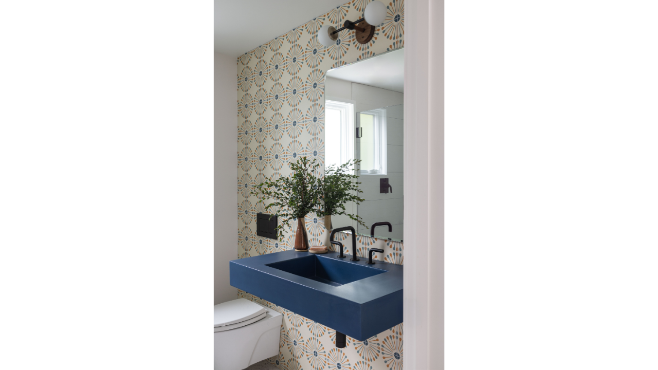 The Shed Buoy’s powder room pairs a sculptural navy-blue sink with matte black fixtures, patterned wallpaper, and a modern globe sconce. The compact space brings bold color and playful detail into the contemporary Portage Bay floating home.