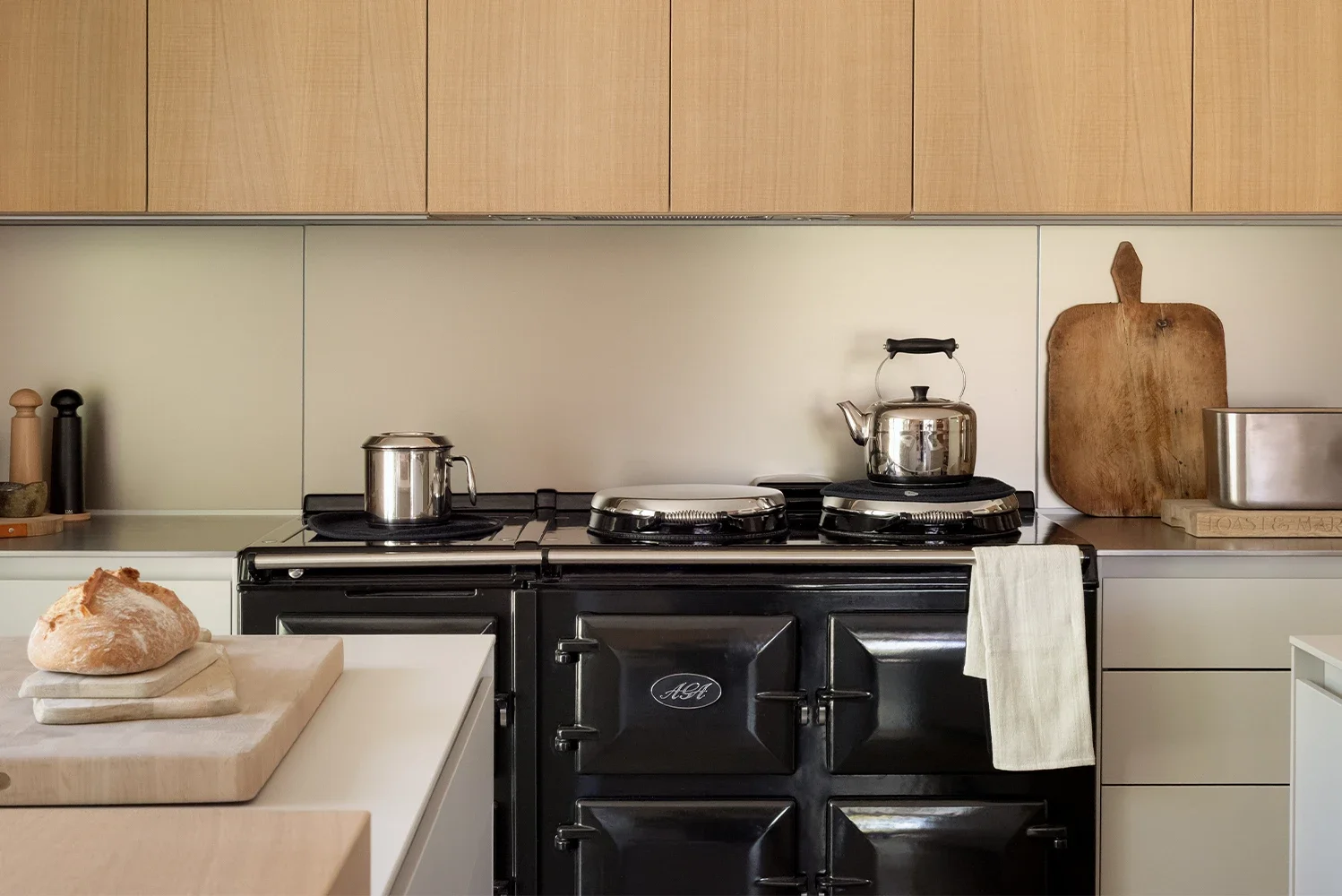 Black AGA framed by light oak bulthaup cabinetry and sand beige aluminium wall panels