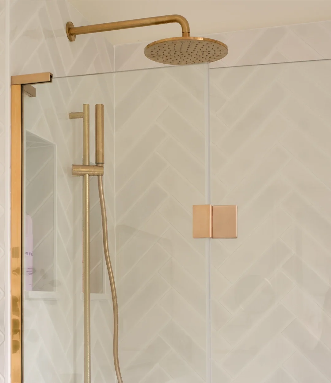 Brushed brass shower enclosure with white herringbone tiles and built-in storage niches