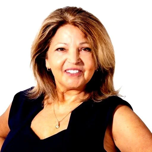 A middle-aged woman with shoulder-length light brown hair, wearing a sleeveless black top and a necklace, smiling against a white background.