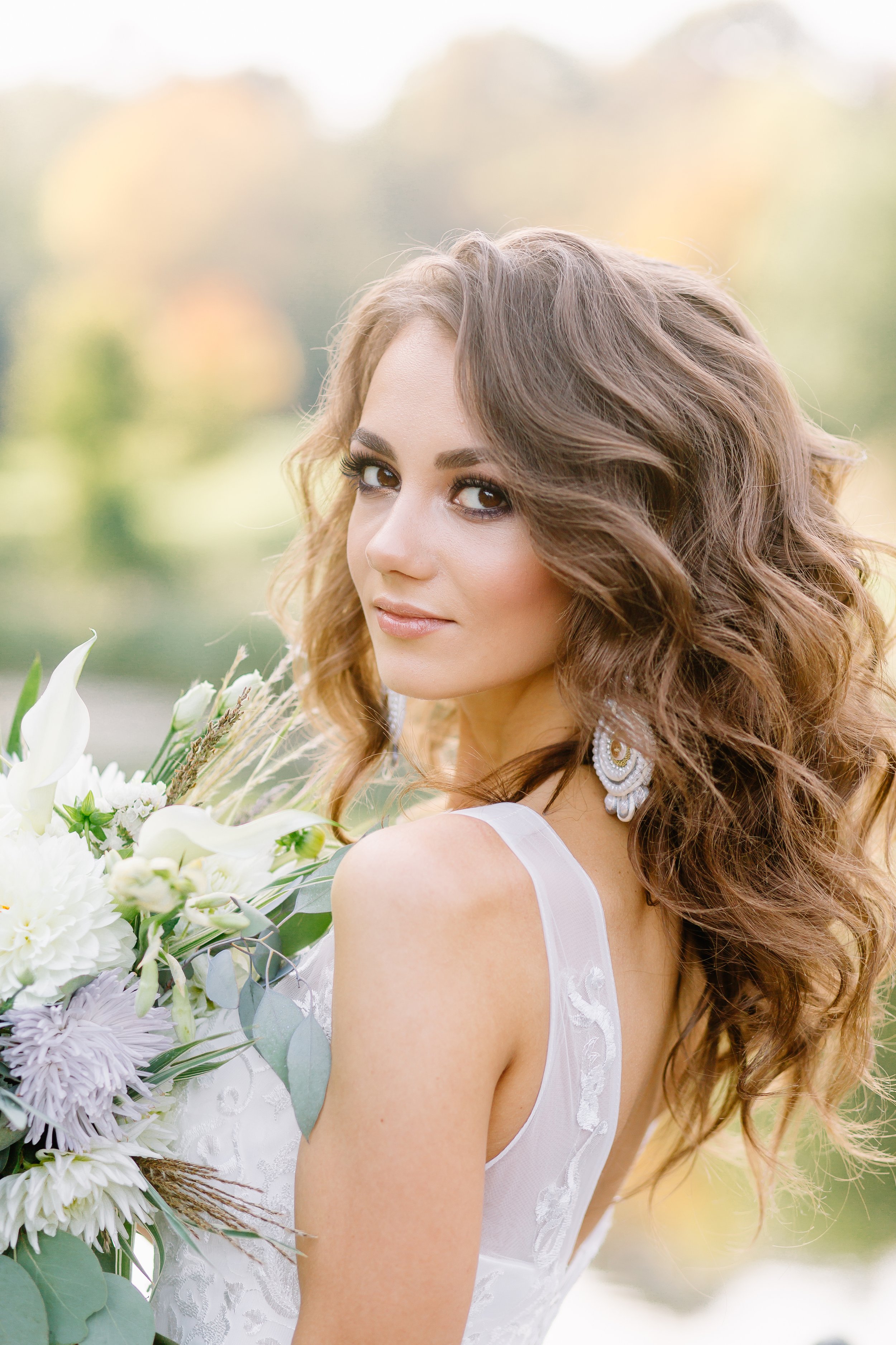 close up of bride with bouquet of soft blue flowers and a lace gown, during a summer wedding.