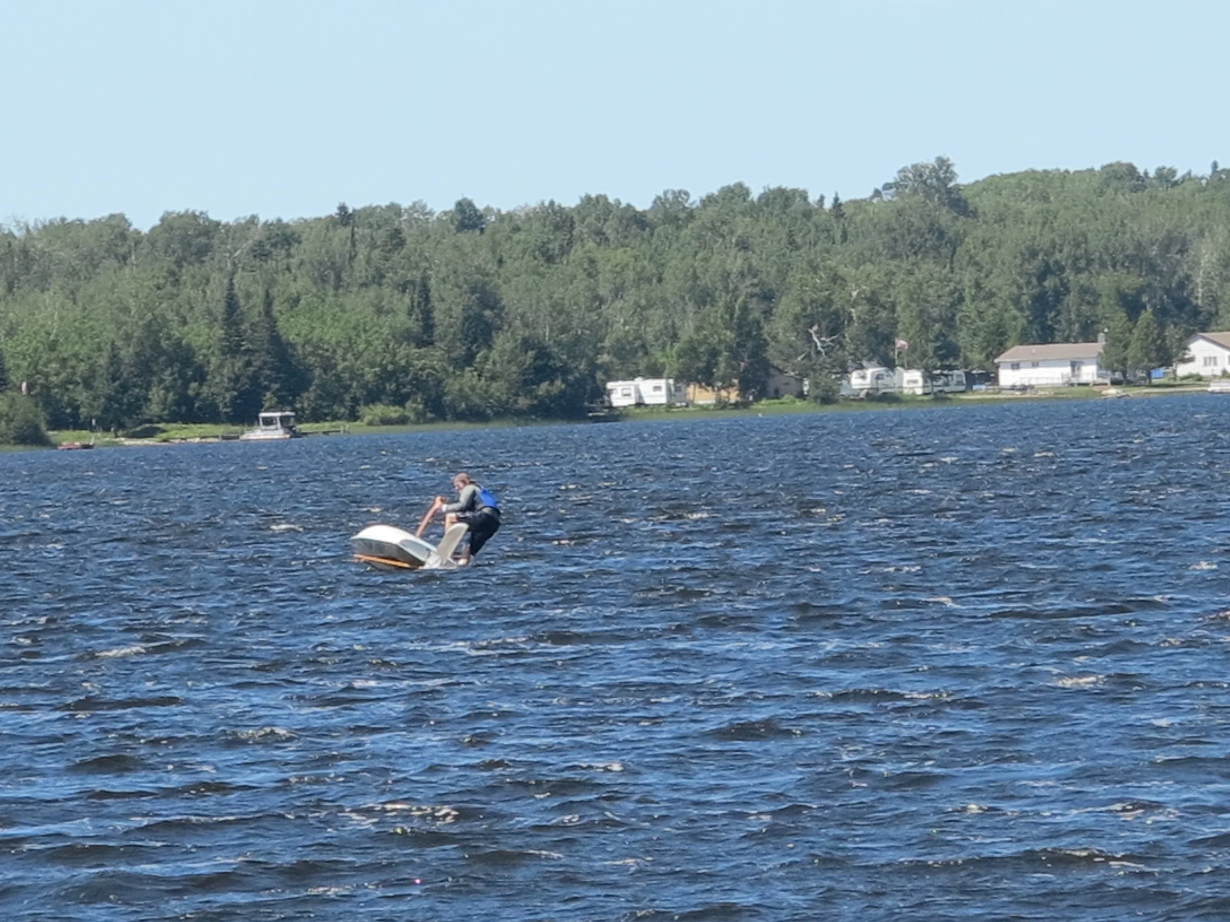 A person riding a jet ski on a lake with a forested shoreline and houses in the background.