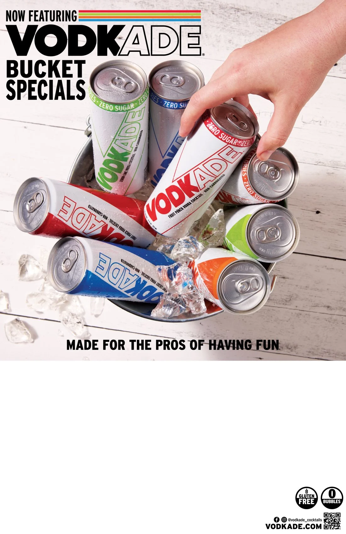 A variety of canned Vodkade drinks in different colors, on ice and in a metal bucket, with a hand grabbing one white can with red lettering, white and red cans with green and blue accents, on a white wooden surface.